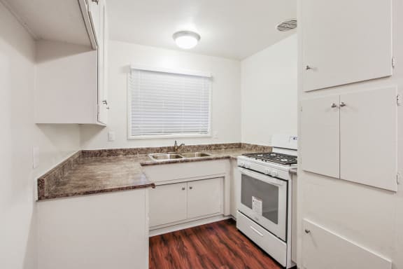 Kitchen with granite countertops, white gas range, white cabinets, and wood style flooring