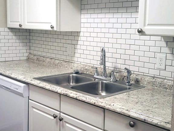 Stainless Steel kitchen sink with white subway tile backsplash and white cabinets at Aspen Run Apartments in Tallahassee, FL
