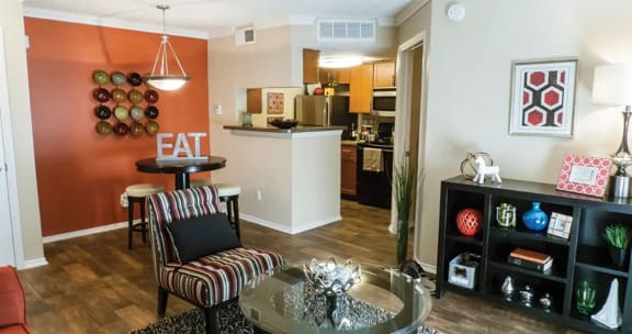 a living room with a table and chairs and a kitchen in the background with hardwood floors at Timberglen Apartments in Dallas, TX