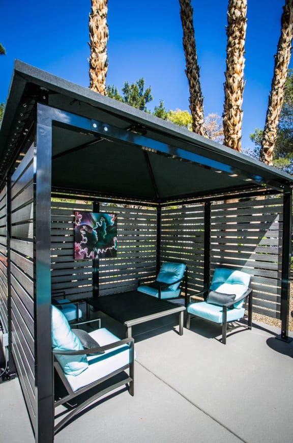Cabana with patio furniture underneath on pool deck with large palm trees in the background,