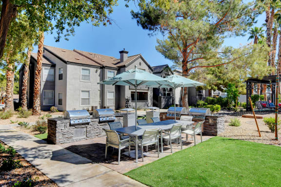 BBQ area grills, trash cans and a large outdoor dinning table with chairs and umbrellas.