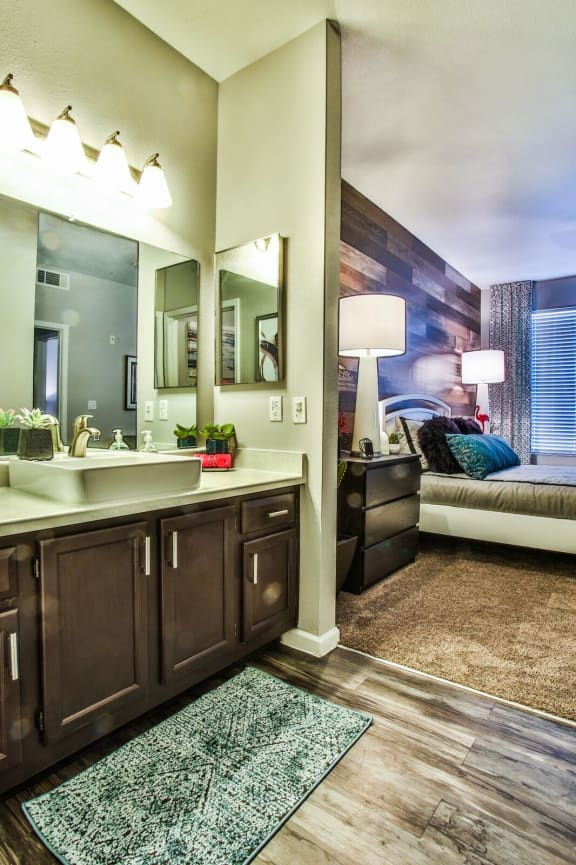 Bathroom with dark cabinets, light counter tops, silver fixtures and the bedroom to the back right.