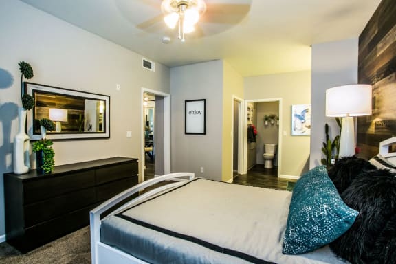 Bedroom with large bed, dresser, wall art and ceiling fan.