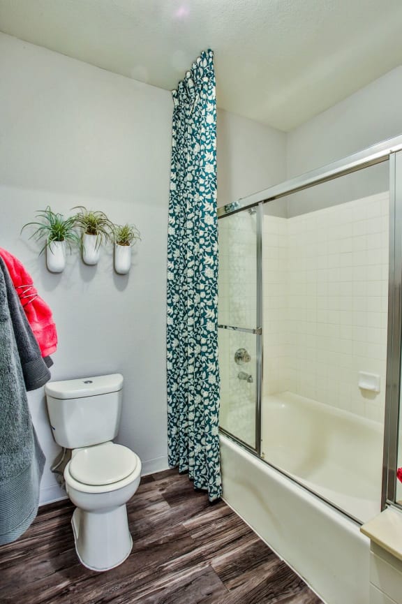 Bathroom with shower/tub combo, white toilet, wood like style flooring and wall décor.