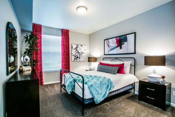 Bedroom with large bed, wall art, carpeting, curtains, two nightstands and two table lamps.
