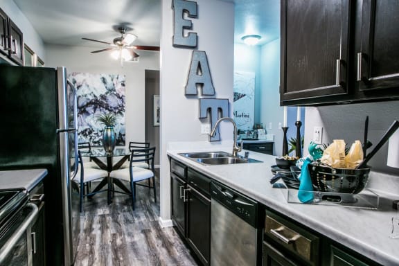 Kitchen with dark cabinets, light countertop, wood like style flooring, stainless steel appliances and the dining room in the background.