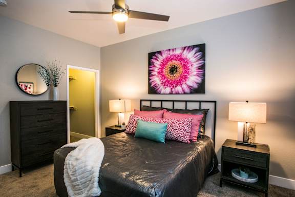 Bedroom with large bed, two nightstands, table lamps, throw blanket, tall dresser, ceiling fan, wall art and carpeting.