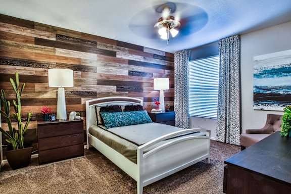 Bedroom with large bed, accent wall, two nightstands, two table lamps, curtain, dresser, ceiling fan and carpeting.
