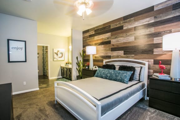 Bedroom with large bed, night stand, table lamp, accent wall and the bathroom to the left back.