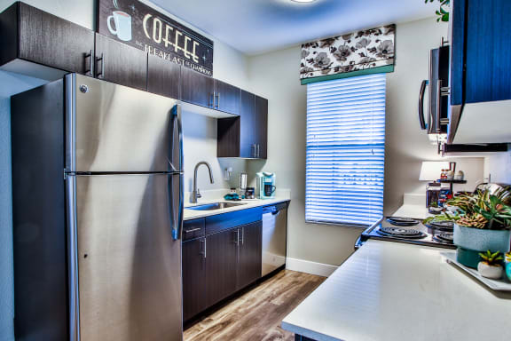 Kitchen with stainless steel appliances, dark cabinets, light color countertops, and wood like style floors.