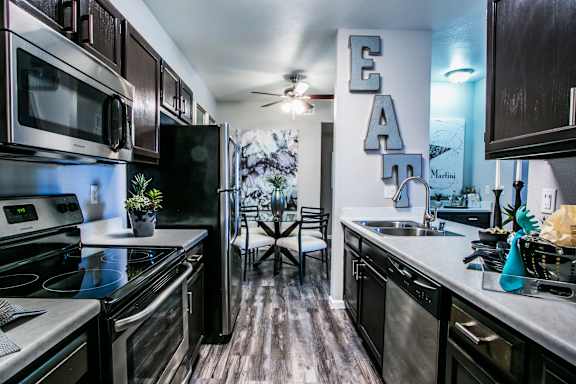 Kitchen with wood like style flooring, stainless steel appliances, dark cabinets, light counter tops and wall art.