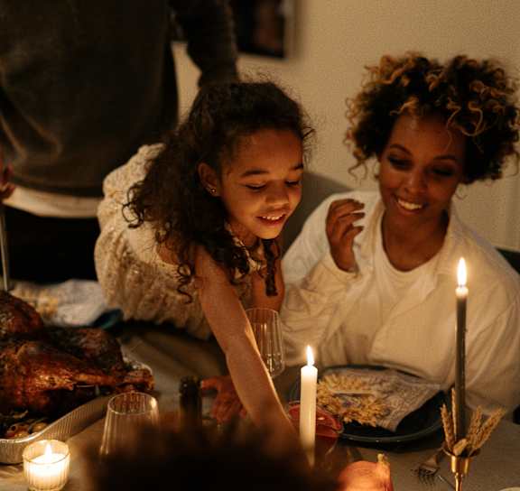 A family is gathered around a dinner table with lit candles.