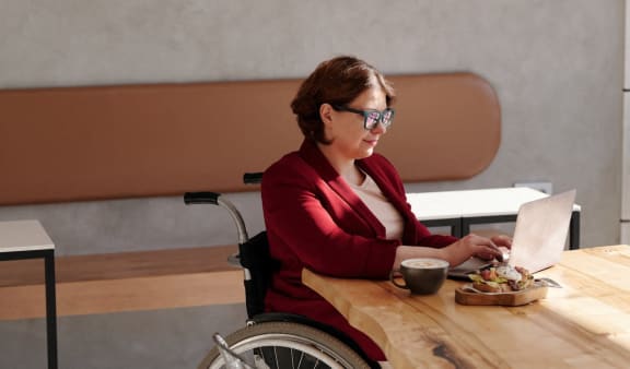 a woman in a wheelchair sitting at a table with a laptop