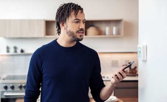 A man in a blue shirt is holding a smartphone in a kitchen.