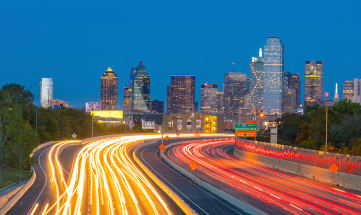 a cityscape of downtown Dallas with blurred lines of traffic in a timelapse of the highway going into the city