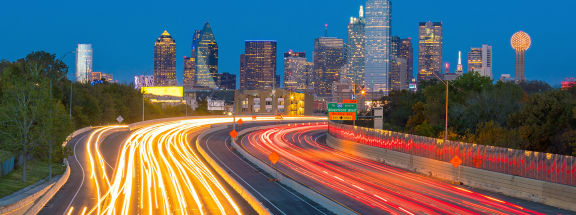 a cityscape of downtown Dallas with blurred lines of traffic in a timelapse of the highway going into the city