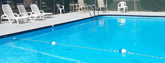 A pool with white lounge chairs and a fence.