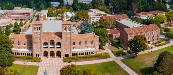 A large building with a green dome is surrounded by smaller buildings and trees.
