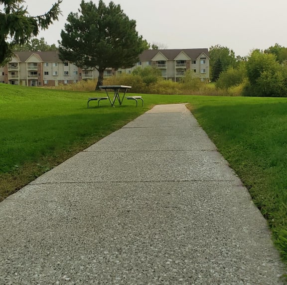 a sidewalk leading to a park with houses in the background