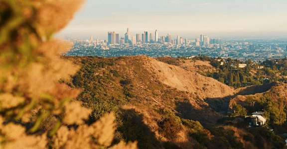 A city skyline is visible through a natural landscape.