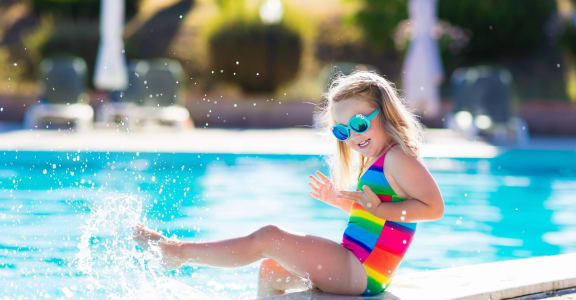 Little Girl in Sunglasses Sitting on Edge of Pool Splashing Water with Legs