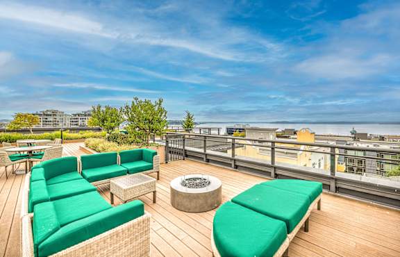A rooftop patio with green couches and a fire pit.