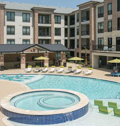 a large swimming pool with lounge chairs in front of an apartment building