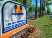 Thumbnail 23 of 23 - Street sign at 9047 San Jose Blvd. Jacksonville, FL 32257 that reads "Mandarin Bay Luxury Apartments" next to row of tall trees and "now leasing" sign.