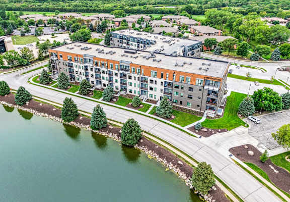 large apartment building with pond in front of it and tons of lush trees