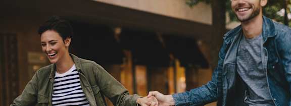 A man and woman are riding bicycles and holding hands.