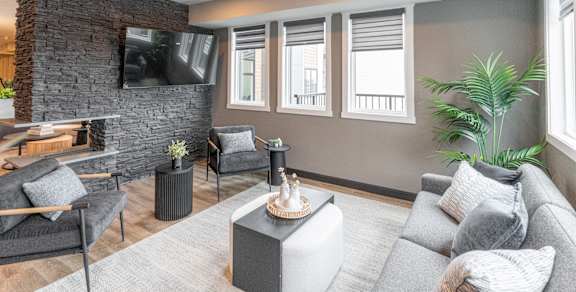 A living room with a grey couch, a black chair, a black coffee table, a stone fireplace, and a flat screen TV mounted on the wall.at Vista Apartments at Edgemont, Edmonton, AB T6M 1J4