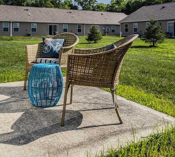 A chair with a blue cushion is placed on a concrete slab with a grassy area and a building in the background.