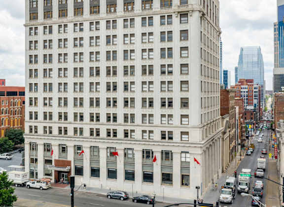 A large white building with many windows is in the middle of a city street.