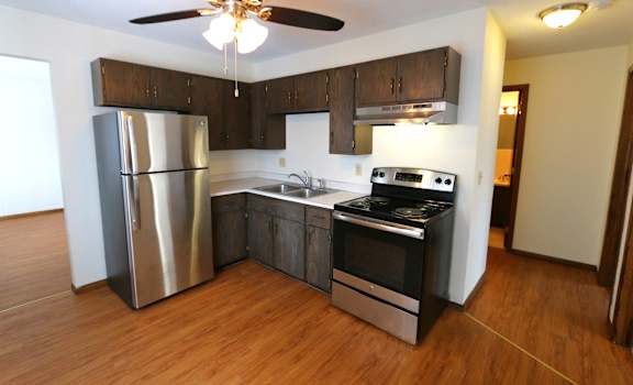 an empty kitchen with stainless steel appliances and wooden floors