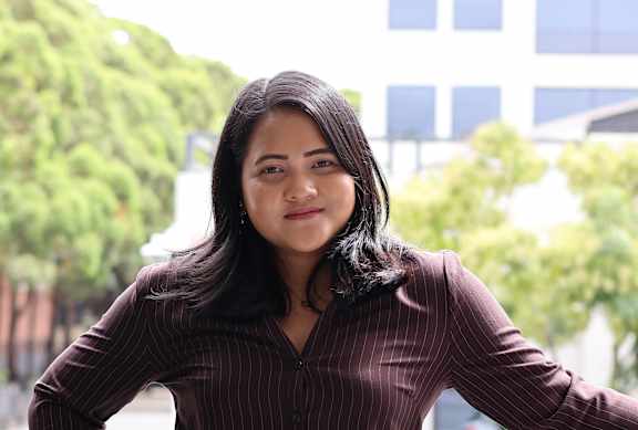 A woman in a brown striped dress leans on a black metal fence.