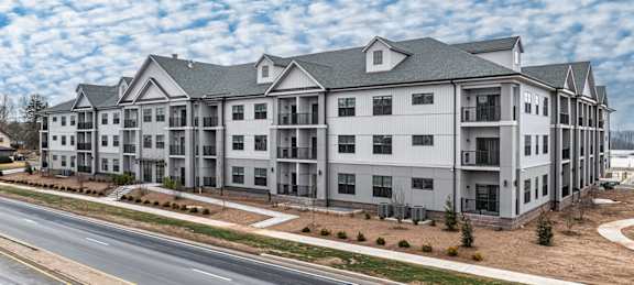 A large, modern apartment building with multiple balconies and a parking lot in front.