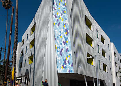 A woman stands in front of a building with a large mosaic on the side.