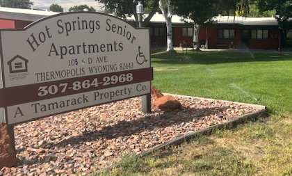 A sign for Hot Springs Senior Apartments is in front of a grassy area.