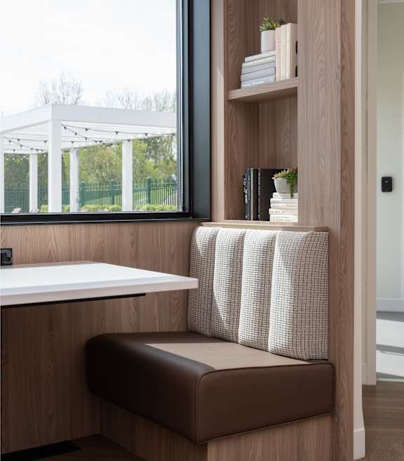 A brown bench with a white cushion is in front of a window.