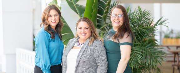 three women standing in front of a large plant