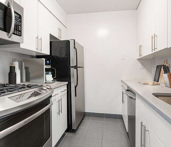 A modern kitchen with stainless steel appliances and white cabinets. at The Ellington Apartments, New York, New York