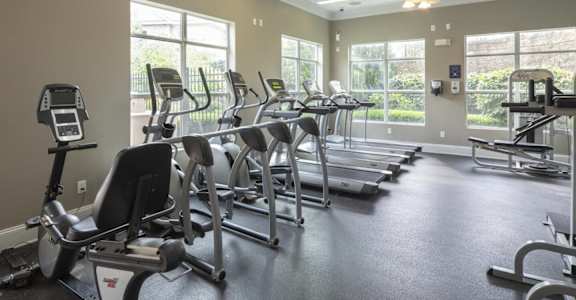 A spacious gym with treadmills, elliptical machines, and a ceiling fan.