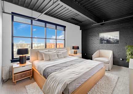 A bedroom with a large bed and a chair.at Plant 1 Lofts, N. Newton