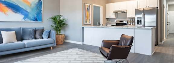 A modern living room with a grey sofa, a brown leather chair, and a kitchen area in the background at Club Villas Apartments, Kathleen, GA, 31047