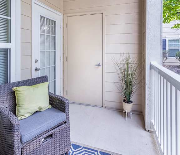 A balcony with a wicker chair and a pillow.