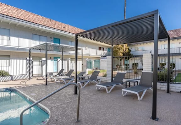 A pool area with sun loungers and a building in the background.