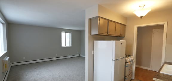 an empty kitchen and living room with a refrigerator and cabinets