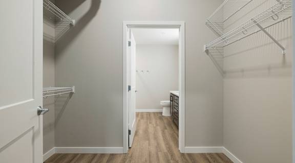 A walk-in closet with white shelves and a wooden floor.