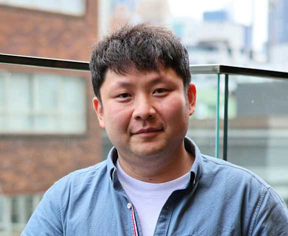 A man in a blue shirt stands on a balcony.
