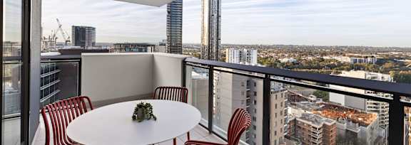 A balcony with a table and chairs overlooking a cityscape.